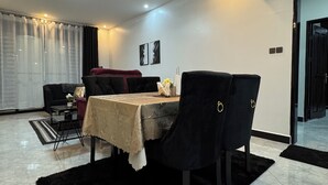 A modern dining area with a table set for two, a black rug, and a sofa.