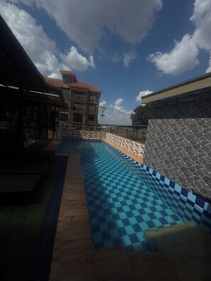 A swimming pool with a checkered pattern, surrounded by a stone wall and a building with a tiled roof.