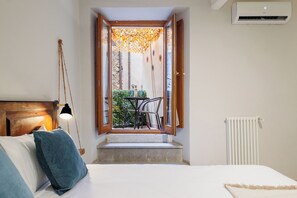 Une chambre à coucher comprenant un lit, une table de chevet, une lampe, une fenêtre avec une porte ouverte donnant sur un balcon et un radiateur.