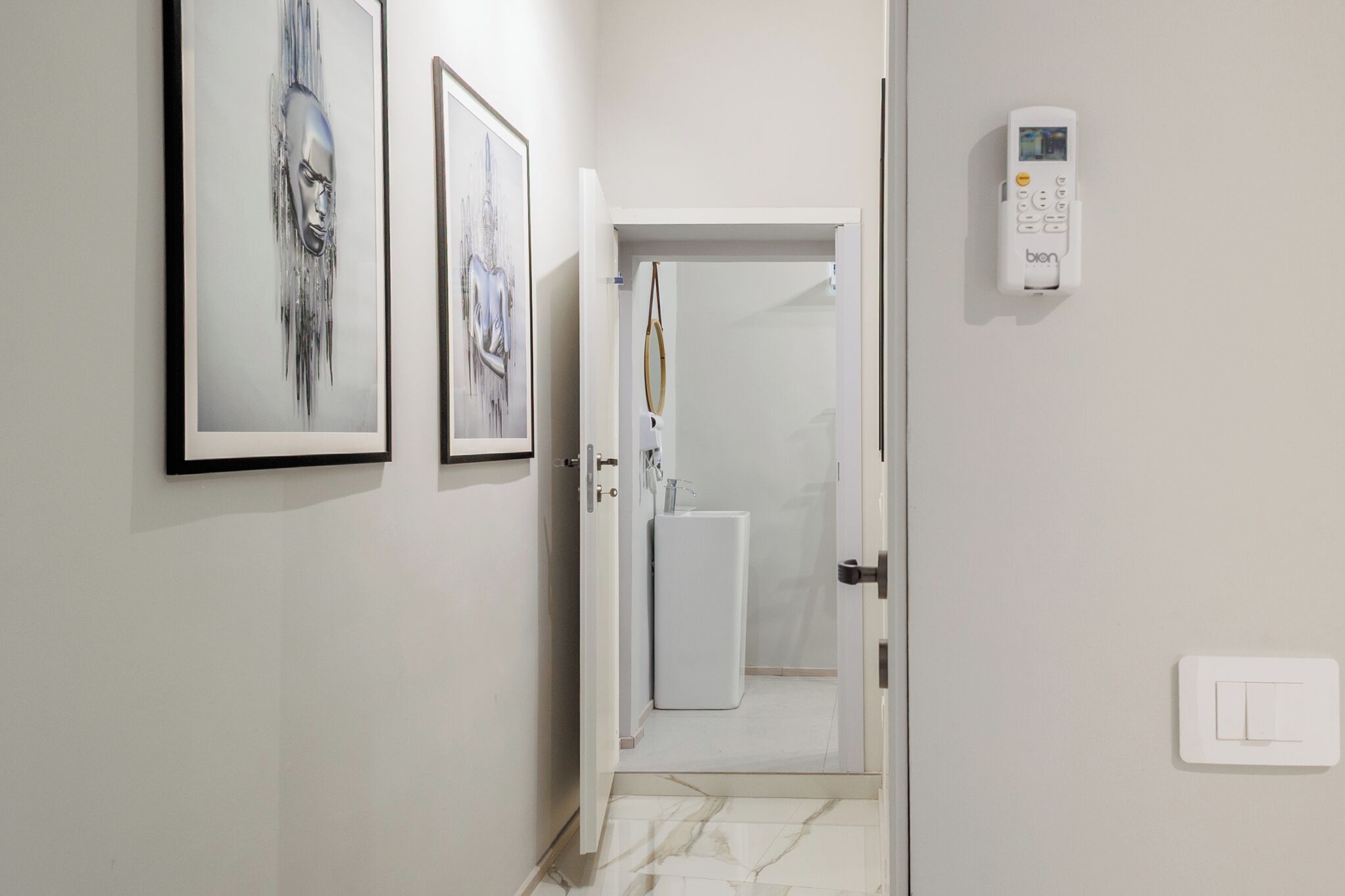 Un pasillo con obras de arte enmarcadas en las paredes, una puerta blanca que da al baño y un termostato en la pared.