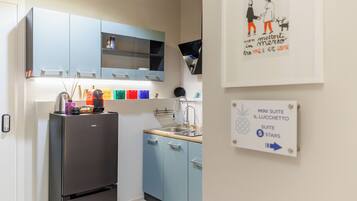 A compact kitchen with a refrigerator, a sink, and light blue cabinets. There is a wall-mounted TV and a framed picture with text.