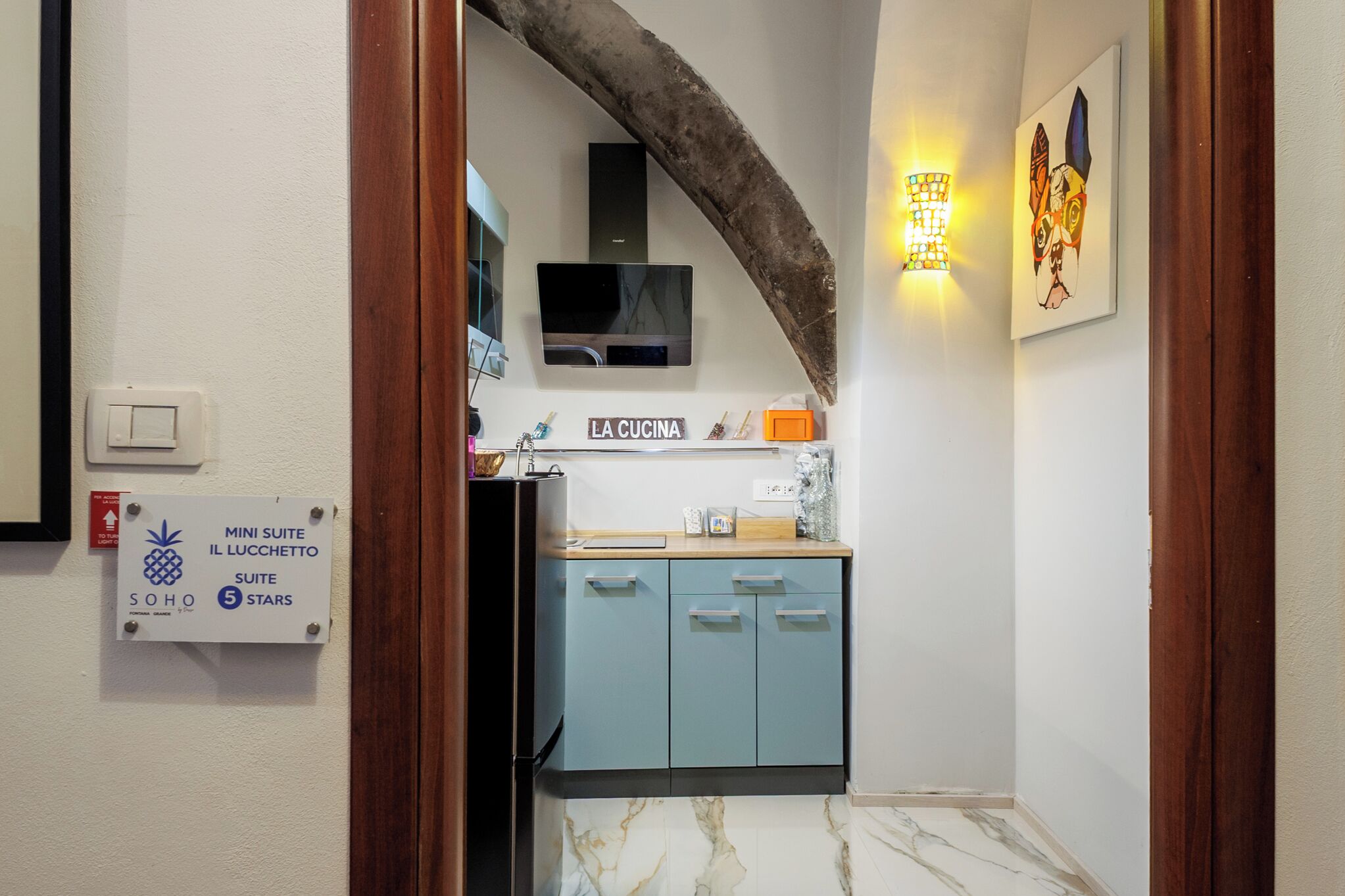 Une cuisine équipée d’un téléviseur, avec une enseigne indiquant « LA CUCINA » et une autre indiquant « MINI SUITE IL LUCCHETTO SUITE 5 ÉTOILES ».