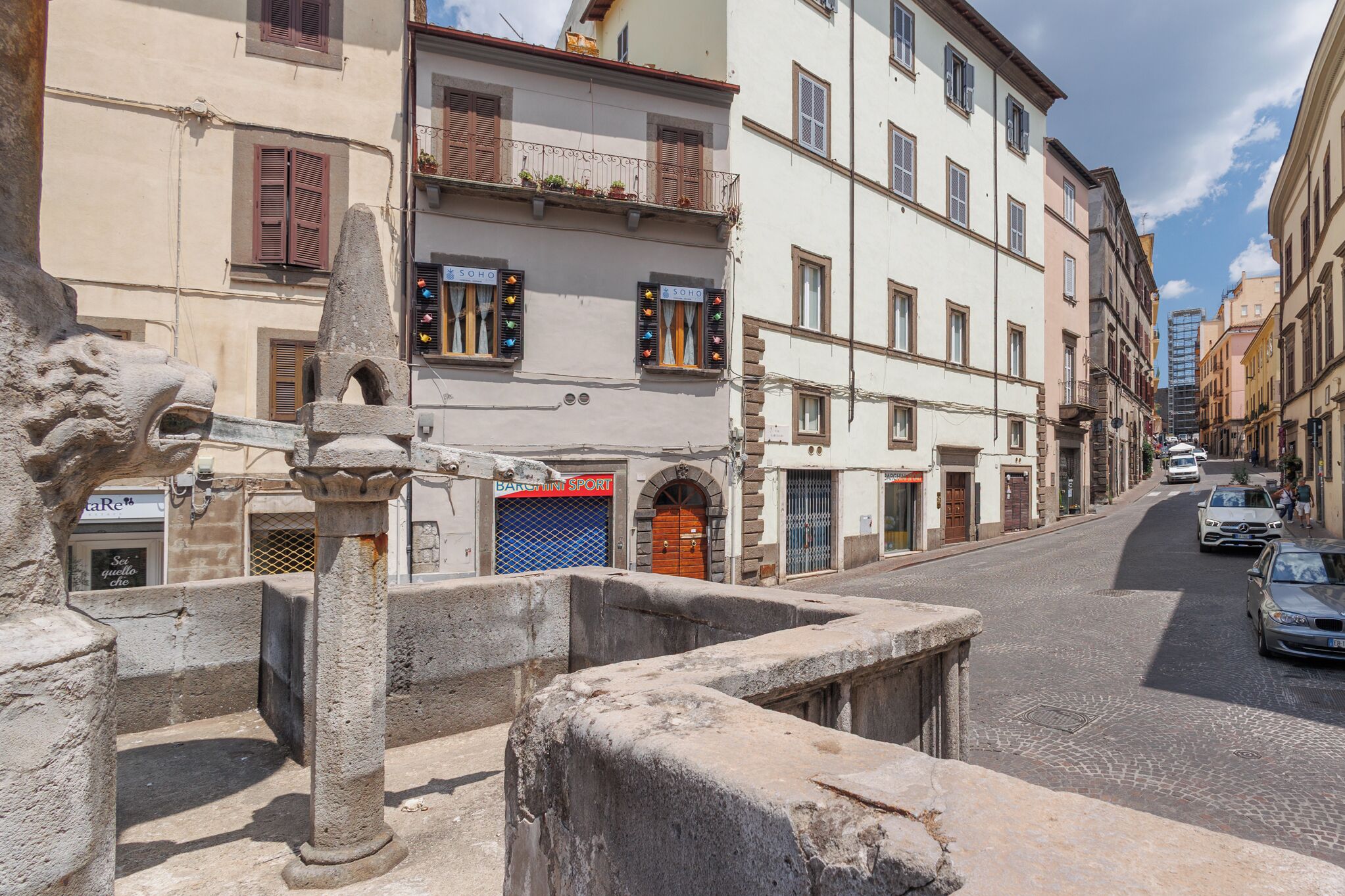 A street with historic buildings, a stone lion statue, and a blue shuttered storefront.