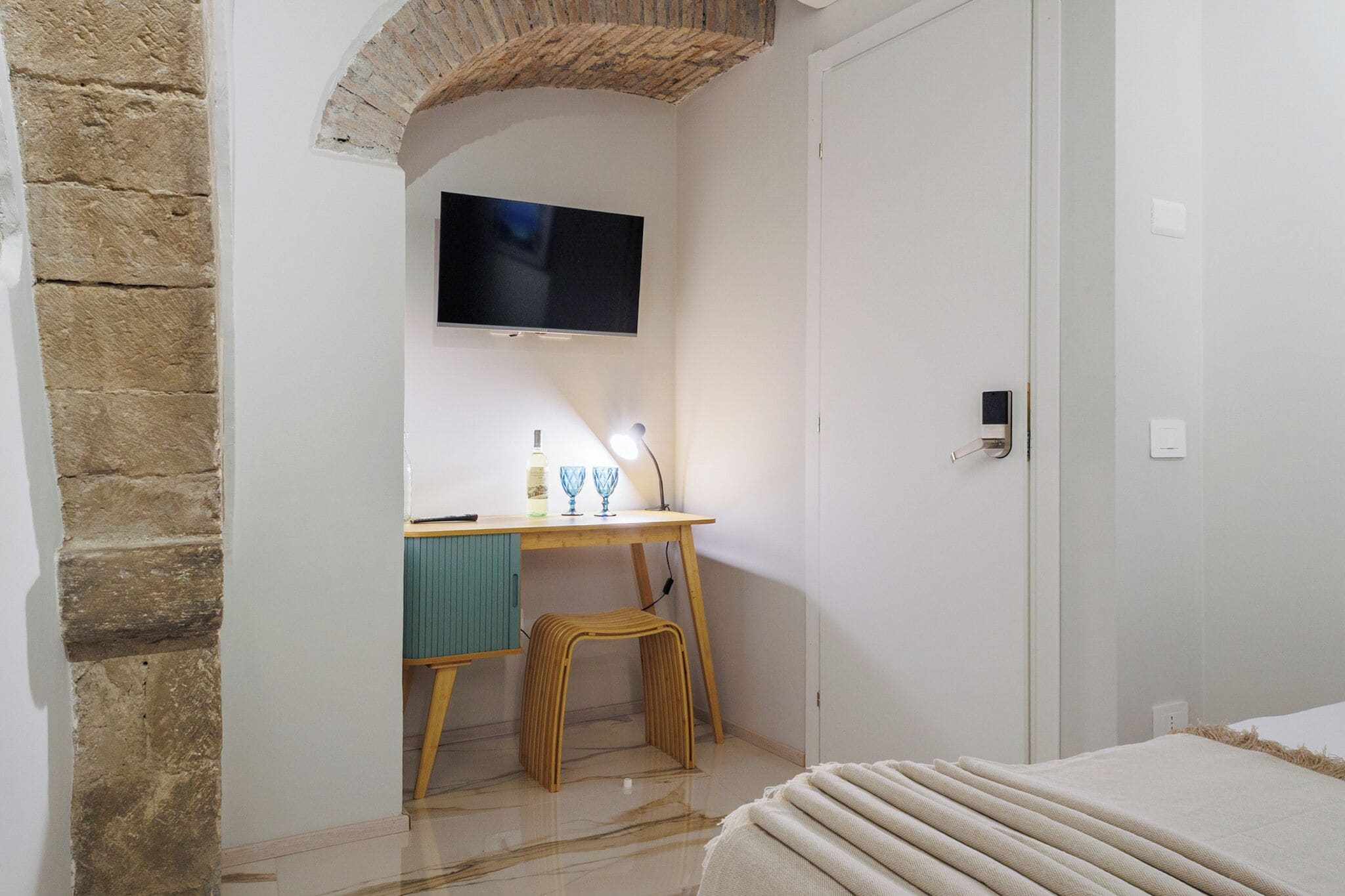 A bedroom with a bed, a desk with a television, and a stone wall.