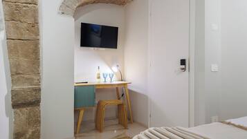 A bedroom with a bed, a desk with a television, and a stone wall.