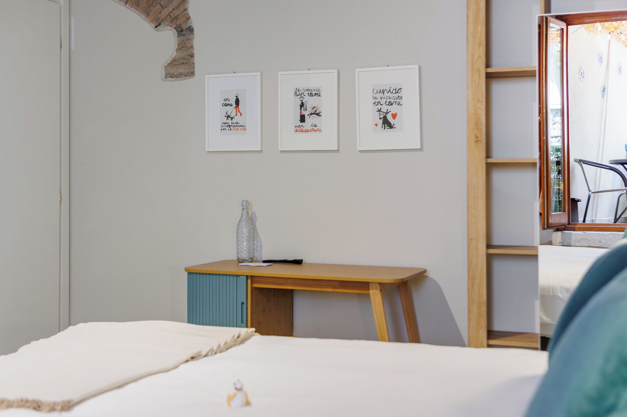 A bedroom with a bed, a desk with a bottle, and three framed artworks on the wall.