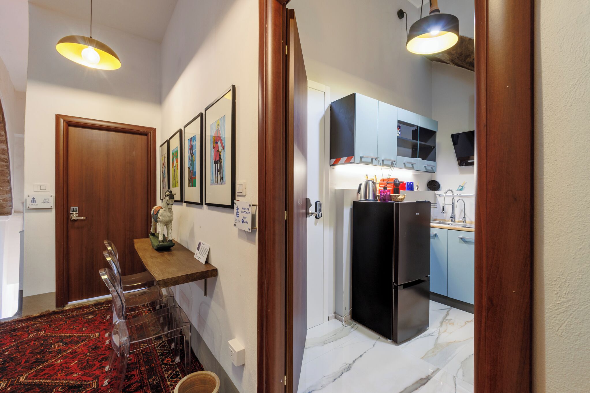 A hallway leading to a kitchen with a refrigerator, a dining area with chairs, and a wooden door.
