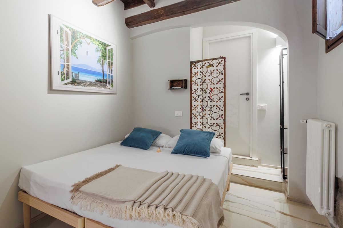 A bedroom with a bed, pillows, a blanket, a painting, a decorative screen, and a radiator.