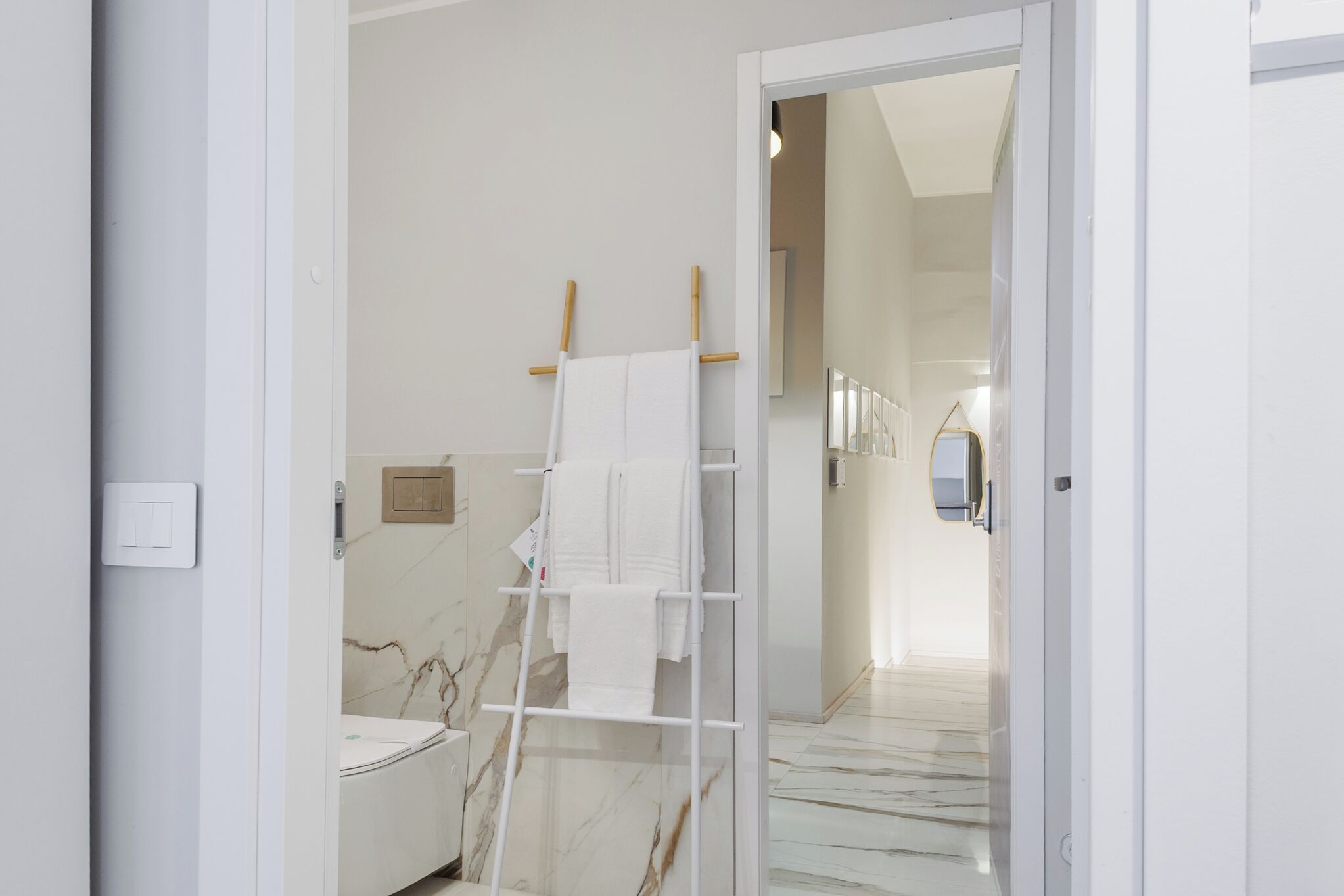 A modern bathroom with a marble floor, a white bathtub, and a towel rack with two towels.