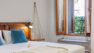 Una cama bien hecha con cabecera de madera, un columpio colgante y una ventana con contraventanas.
