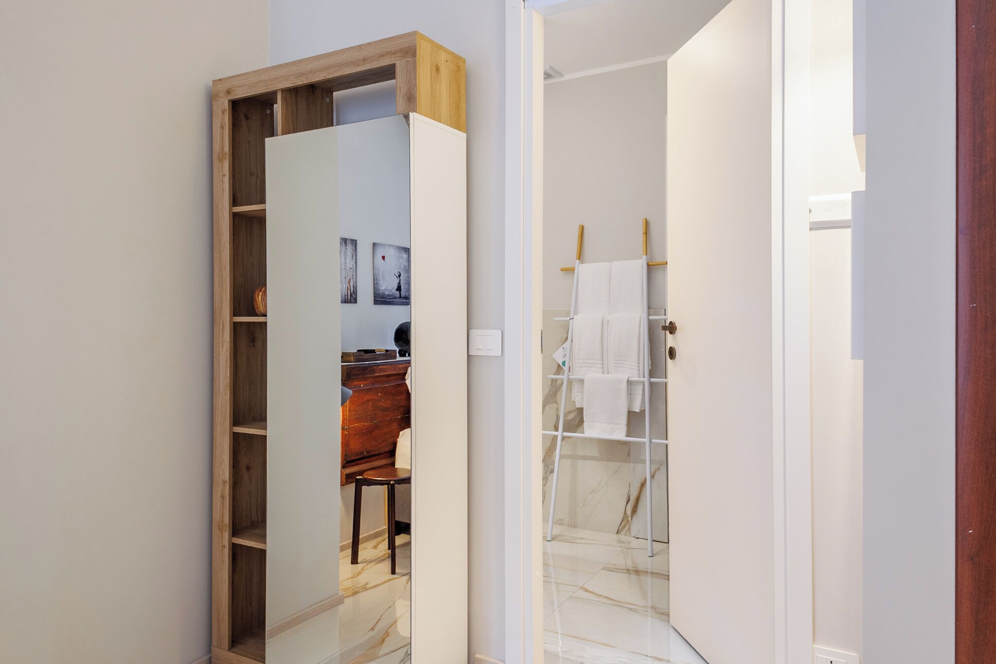 A modern bathroom with a wooden vanity, marble flooring, and a towel rack.