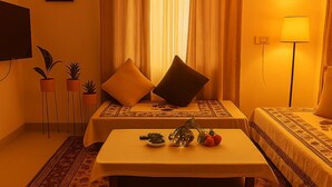 Ein Zimmer mit zwei Betten, einem Tisch mit Vase und Obst, einem Fernseher an der Wand und einer Lampe.