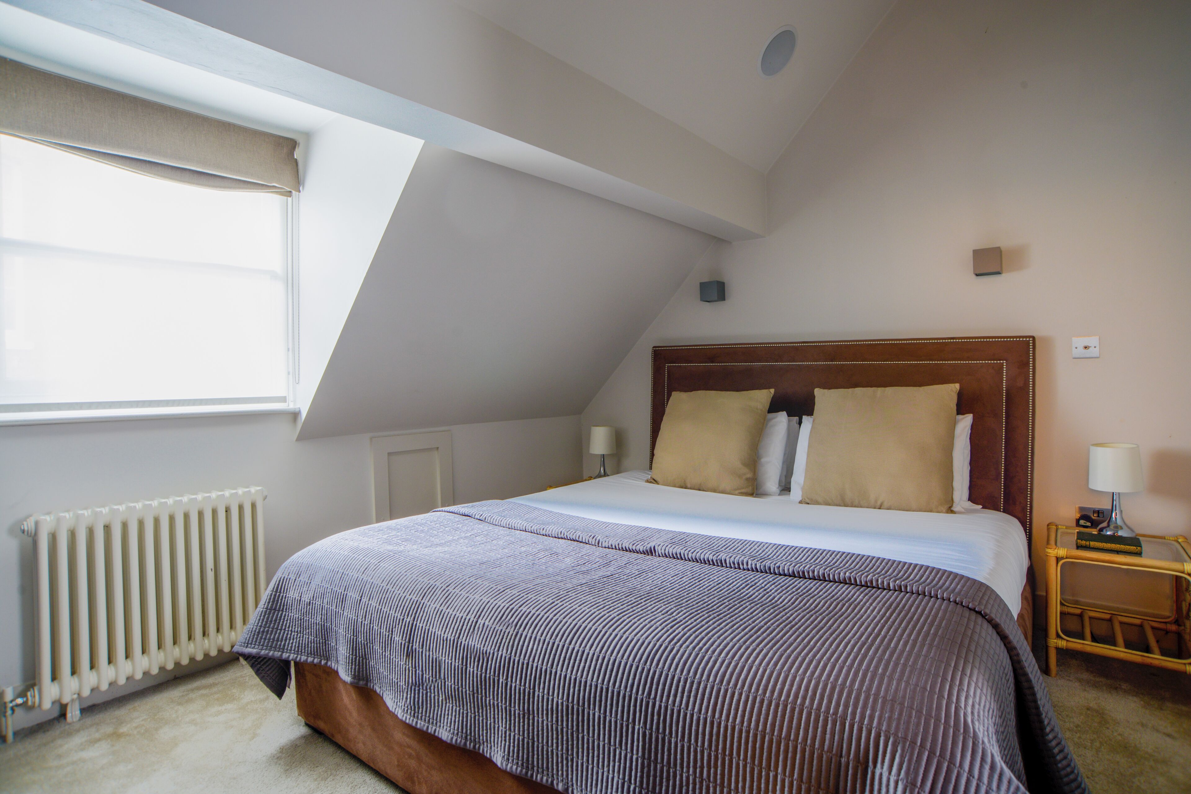 A bedroom with a large bed, a wooden headboard, a nightstand with a lamp, and a window with a curtain.