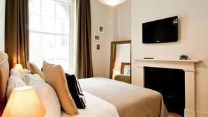 Une chambre d’hôtel avec un lit, un téléviseur fixé au-dessus d’une cheminée et une fenêtre avec des rideaux.