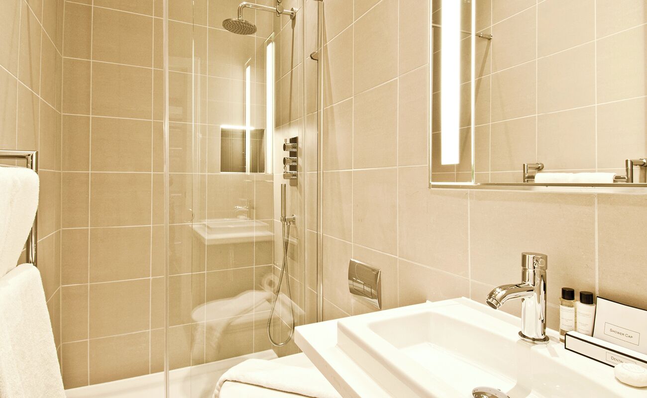 Un baño moderno con ducha envuelta en vidrio, lavamanos blanco y espejo sobre él.