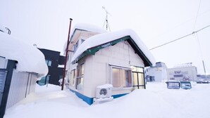 A house partially buried in snow with a visible air conditioning unit and a satellite dish. - Nordic House (Furano)