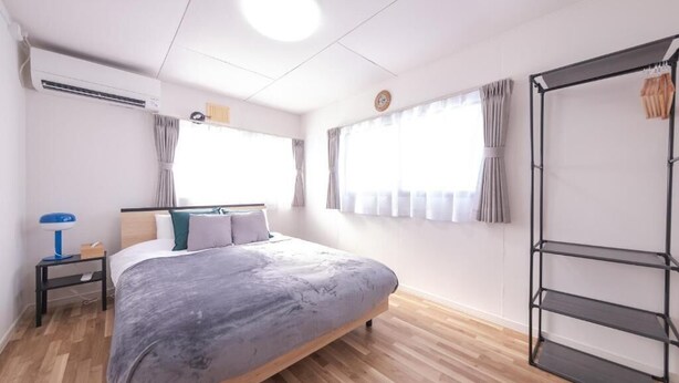 A bedroom with a bed, a wardrobe, a nightstand, and a window with curtains. - Nordic House (Furano)