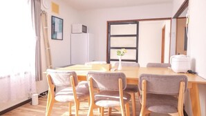 A dining area with a wooden table and four chairs, a potted plant, and a large window with curtains. - Nordic House (Furano)