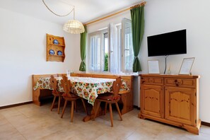 A dining area with a table, chairs, a wooden cabinet, a television, and a window with curtains.