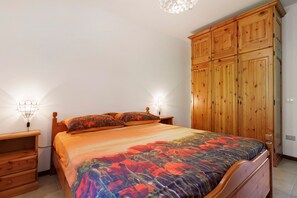 A bedroom with a bed, wooden wardrobe, nightstands, and wall-mounted lamps.