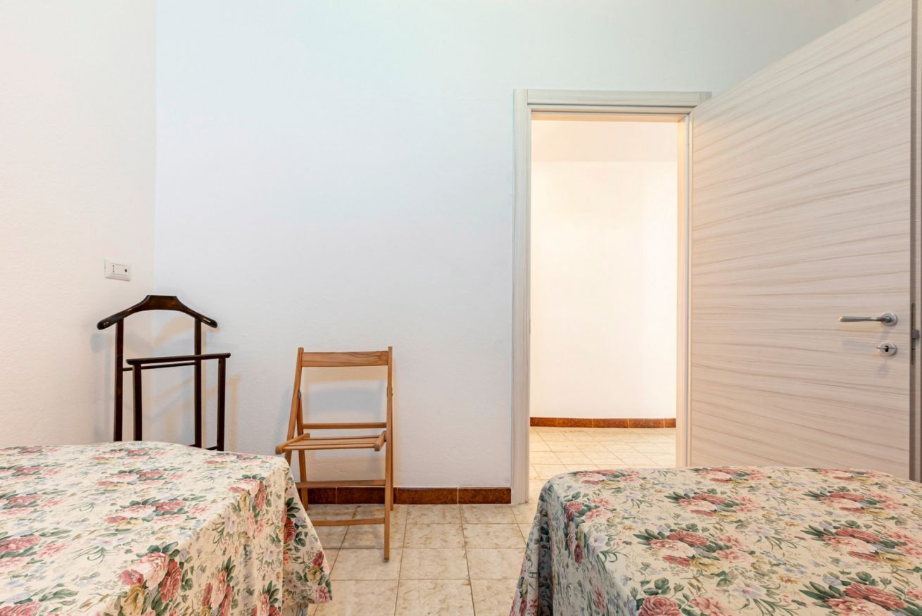 A room with two beds, a chair, a wardrobe, and a door leading to another room.