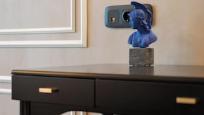 A desk with a blue sculpture, a power outlet, and a brown ottoman. - Athena Suite by Acropolis Luxury Athens Suites (Athens)