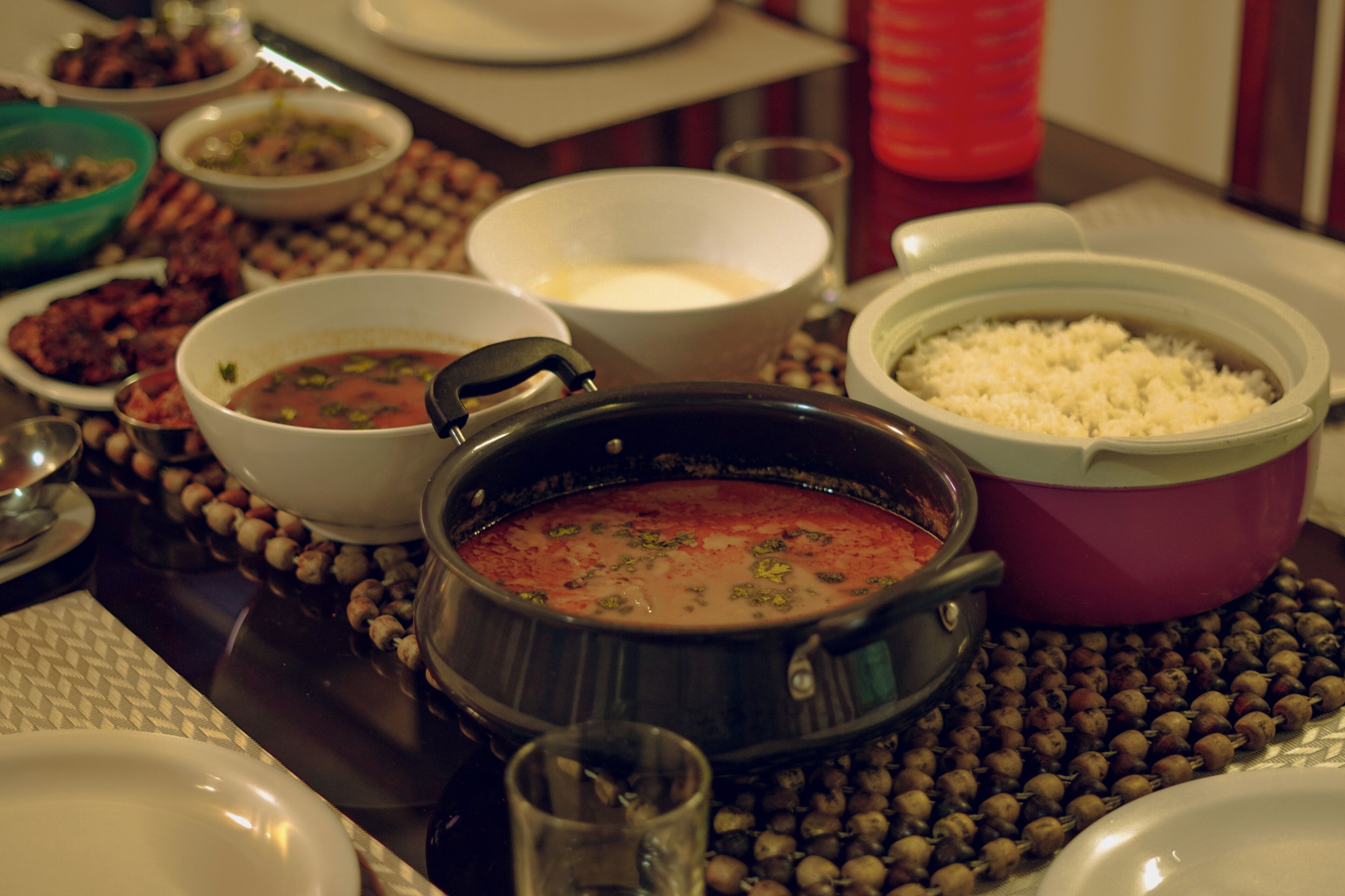 A table with various dishes including a pot of soup, a bowl of rice, and several side dishes.