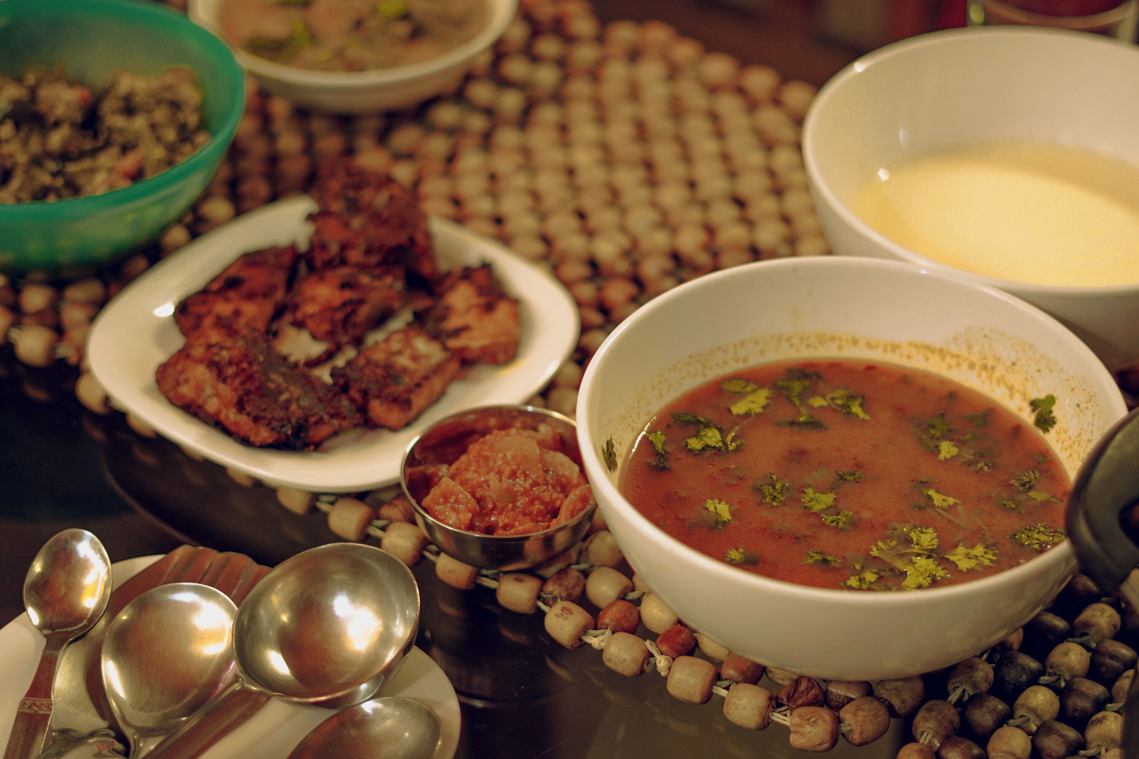 Une table dressée avec différents plats, notamment un bol de soupe, une assiette de viande et un bol de sauce.