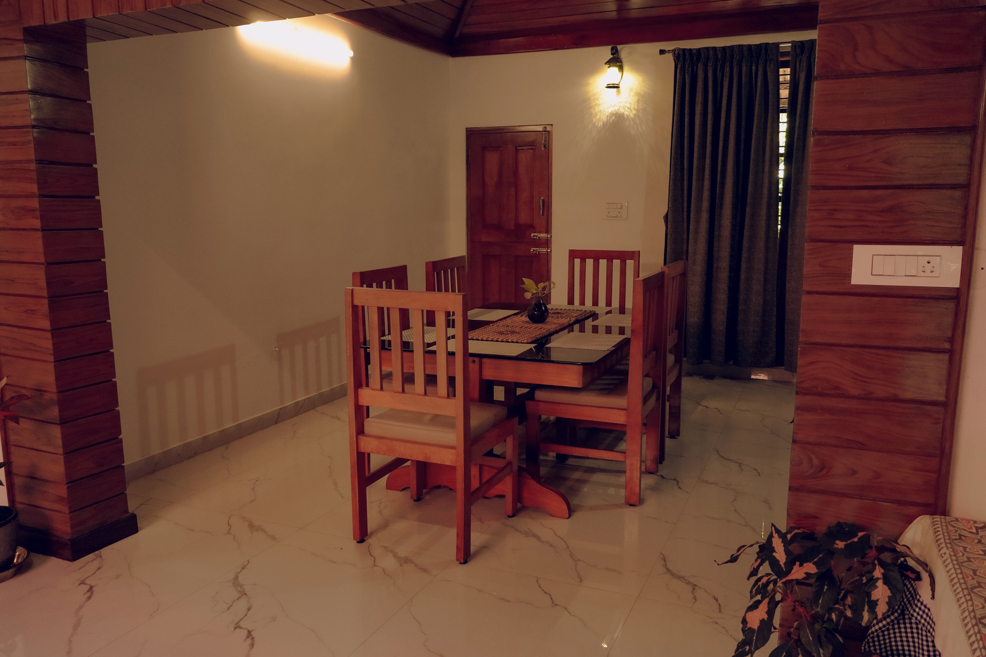 A dining area with a wooden table and chairs, a vase with a plant, and a door leading to another room.