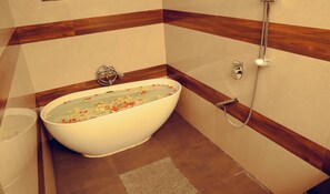 Ein Badezimmer mit einer freistehenden Badewanne, gefüllt mit Wasser und Blütenblättern, einer Duschbrause und einem Handtuchhalter.