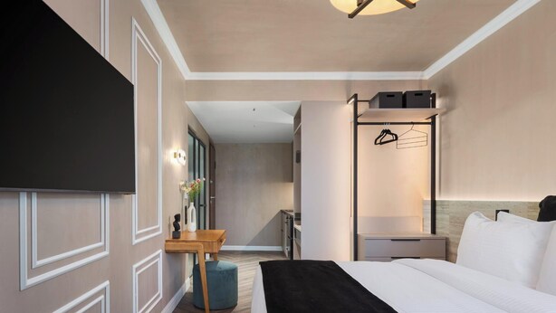 A hotel room with a bed, a desk, a chair, a wardrobe, and a mirror.