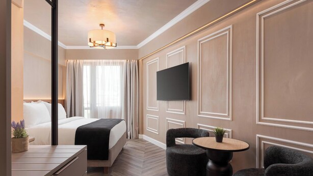 A hotel room with a bed, a desk, two chairs, a TV, and a chandelier. - Aphrodite Suite by Acropolis Luxury Athens Suites (Athens)