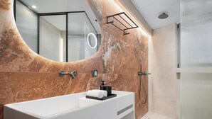 A modern bathroom with a large oval mirror, a white bathtub, and a shower area. - Aphrodite Suite by Acropolis Luxury Athens Suites (Athens)