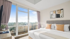 Ein modernes Hotelzimmer mit großem Fenster, einem Bett mit weißer und orangefarbener Bettwäsche, einem grauen Kopfteil und zwei abstrakten Wandbildern.