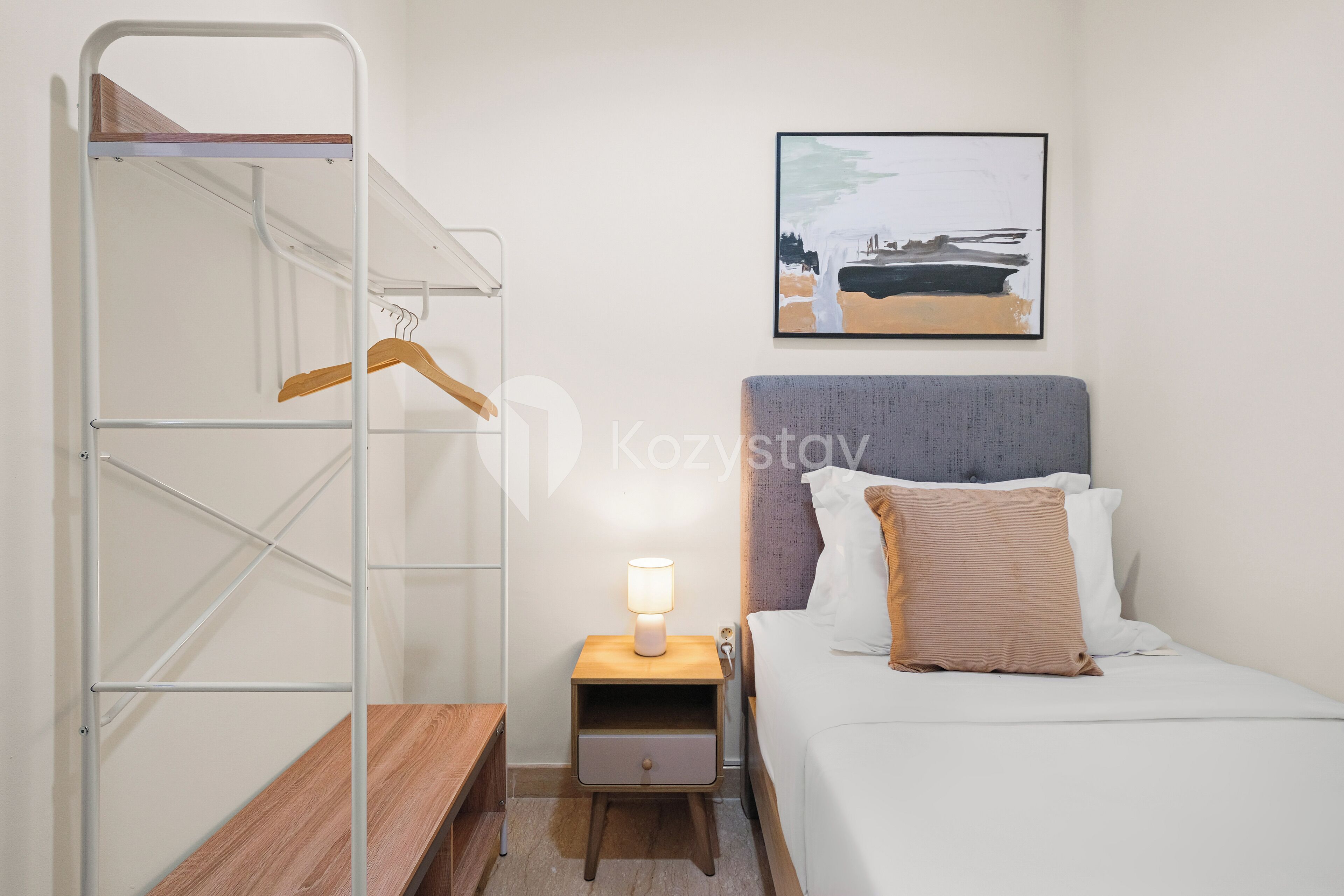 A compact hotel room with a bunk bed, a bedside table with a lamp, a small drawer, and a framed picture on the wall.