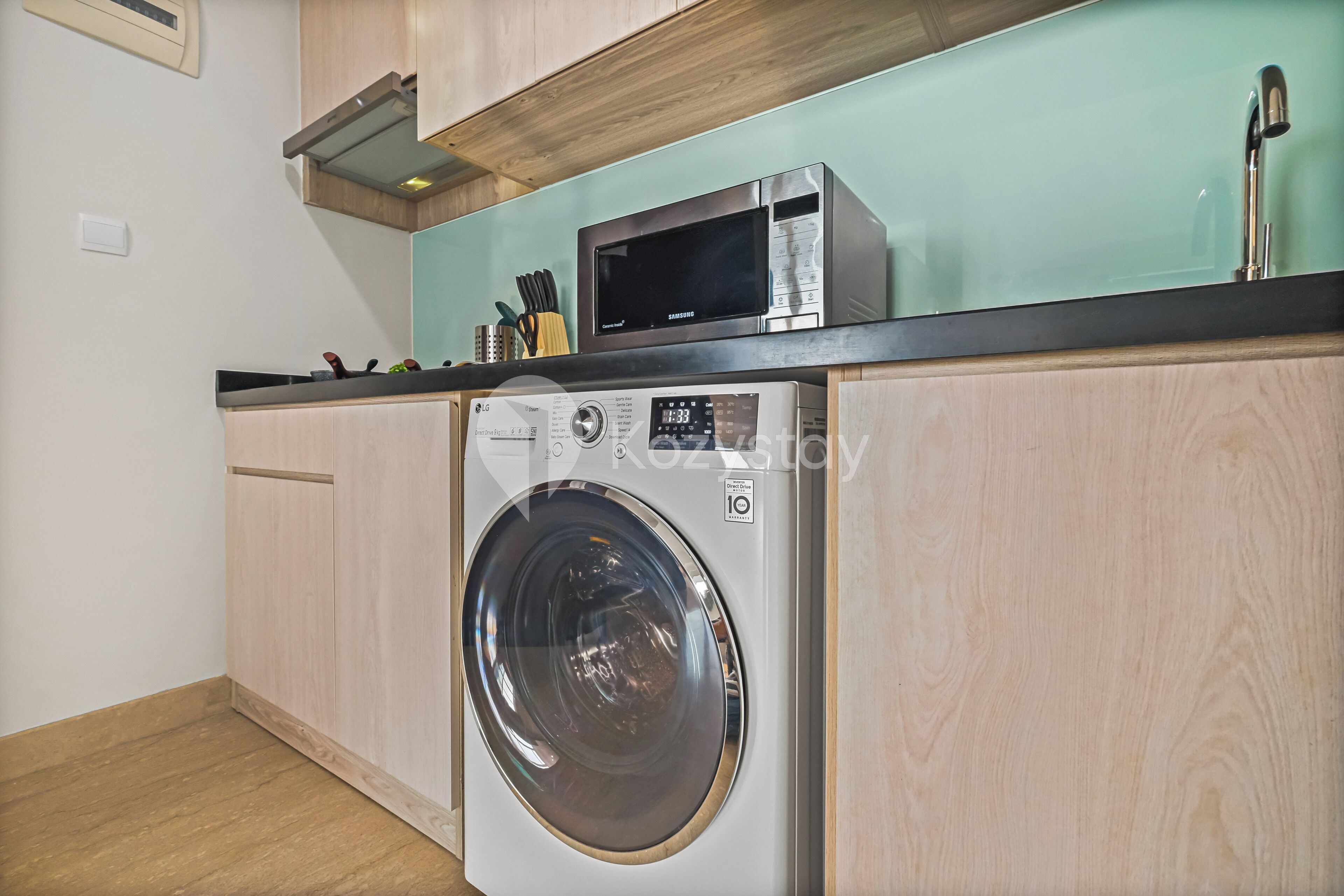 A compact kitchen with a washing machine, microwave, and wooden cabinets.