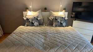 A neatly made bed with a quilted duvet, two bedside tables with lamps, and a flat-screen TV on a stand. - Vacation apartment in Warwerort near Büsum (Warwerort)