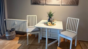A dining area with a white table and chairs, a vase with plants, and three framed pictures on the wall. - Vacation apartment in Warwerort near Büsum (Warwerort)