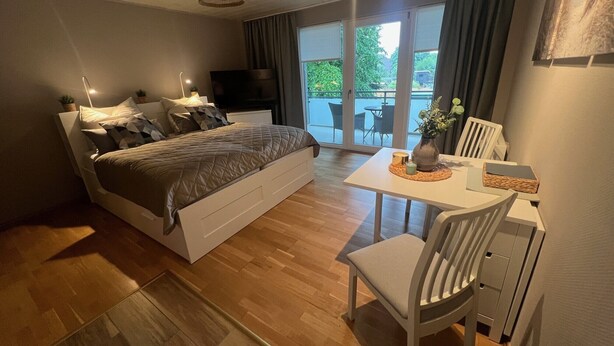 A bedroom with a bed, bedside tables, a desk, and a chair. There is a window with curtains, a ceiling light, and a view of the outdoors. - Vacation apartment in Warwerort near Büsum (Warwerort)
