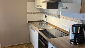 A compact kitchen with white cabinetry, a stainless steel sink, a black stove, and a coffee maker. - Vacation apartment in Warwerort near Büsum (Warwerort)