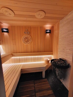 Un sauna avec des bancs en bois, un mur en pierre et un appareil de chauffage en pierre.