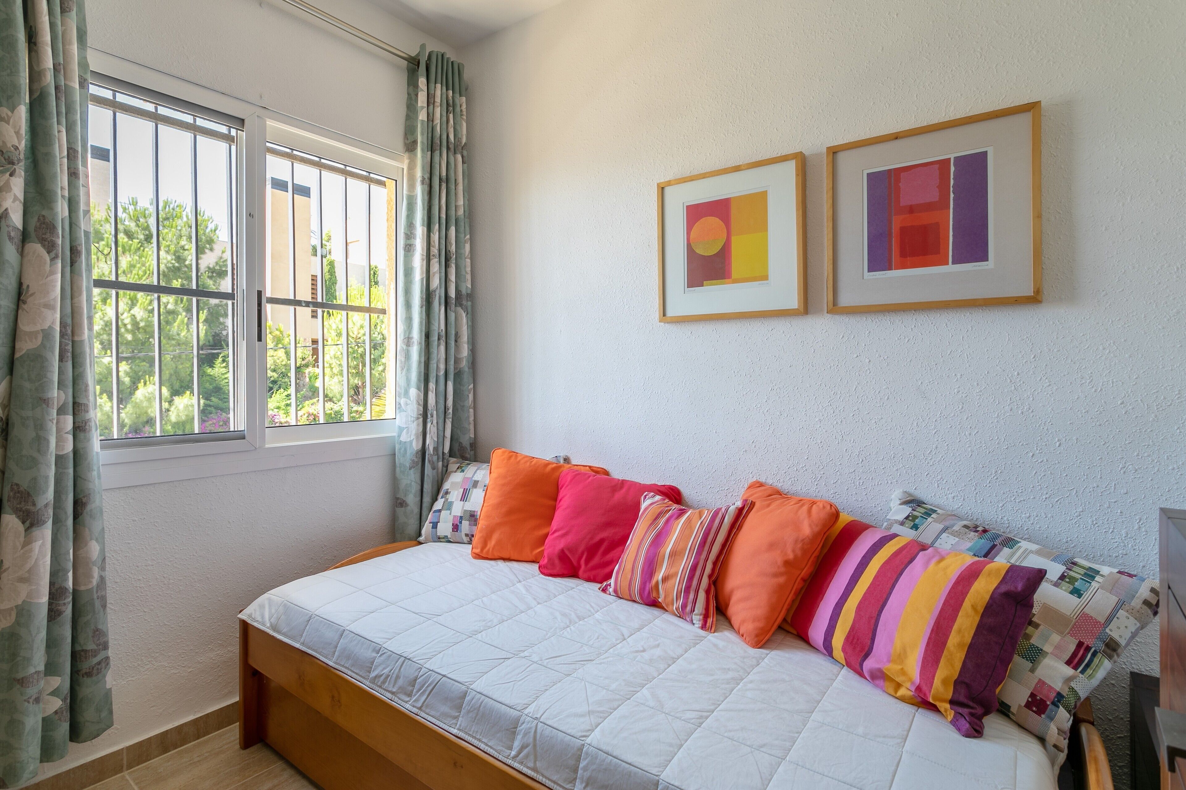 A bedroom with a bed, curtains, and two framed pictures on the wall.