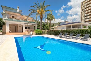 Una piscina con sillas de descanso, un edificio con balcón y palmeras.
