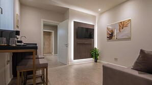 A modern living room with a sofa, a coffee table, and a TV mounted on the wall. There is a door leading to another room and a small plant on the floor. - MODENA RELAX Luxury Rent Rooms (Modena)