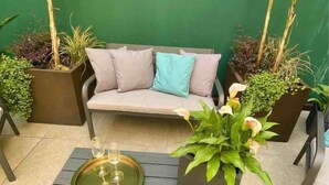 A patio with a grey sofa, two black chairs, a small table with a glass tray, and potted plants. - MODENA RELAX Luxury Rent Rooms (Modena)