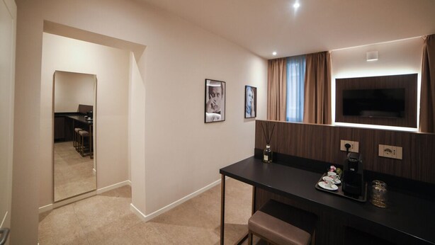 A modern hotel room with a dark wooden desk, a flat-screen TV, and a small seating area. - MODENA RELAX Luxury Rent Rooms (Modena)