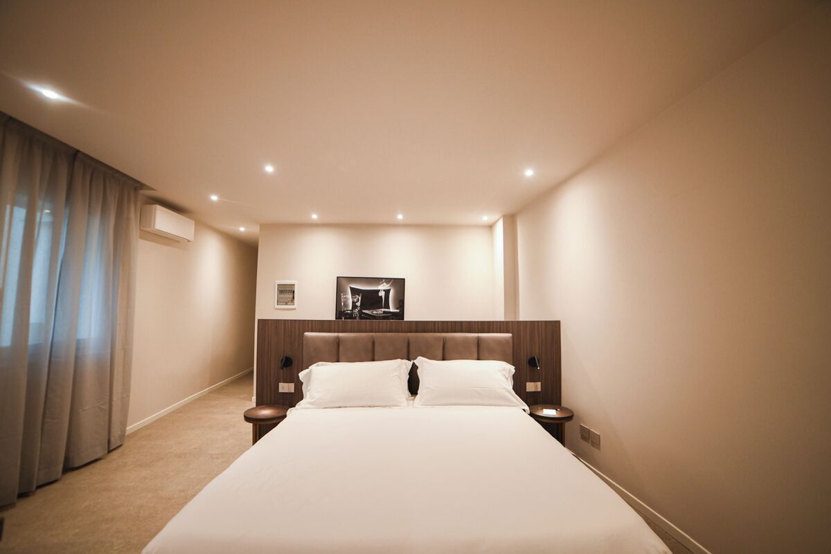 Hotelkamer met een groot bed, hoofdeinde, twee nachtkastjes, een wandtelevisie en een raam met gordijnen.
