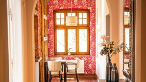 Un pasillo con suelo de madera, un radiador, una mesa con sillas y un jarrón con flores sobre una consola.