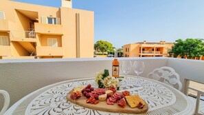 A table with a charcuterie board, a bottle of wine, and glasses on a balcony with a view of buildings. - Apartment 'Golfview' with Shared Pool, Wi-Fi and Air Conditioning (Quarteira)