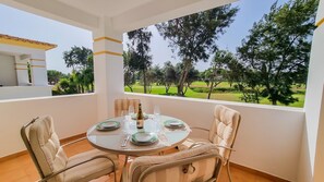 Un coin repas avec une table dressée pour quatre personnes, des chaises et une vue sur un paysage verdoyant, parsemé d’arbres.